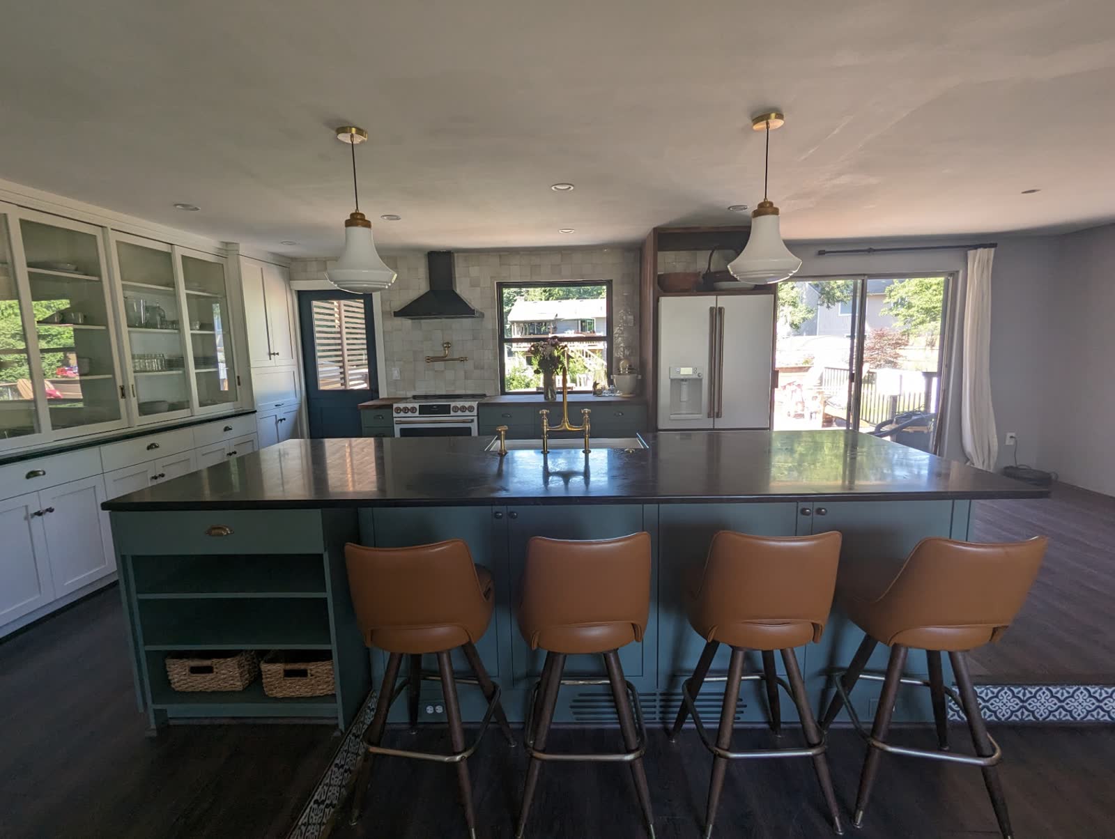 Sage green island kitchen with schoolhouse pendants, leather stools and glass hutch