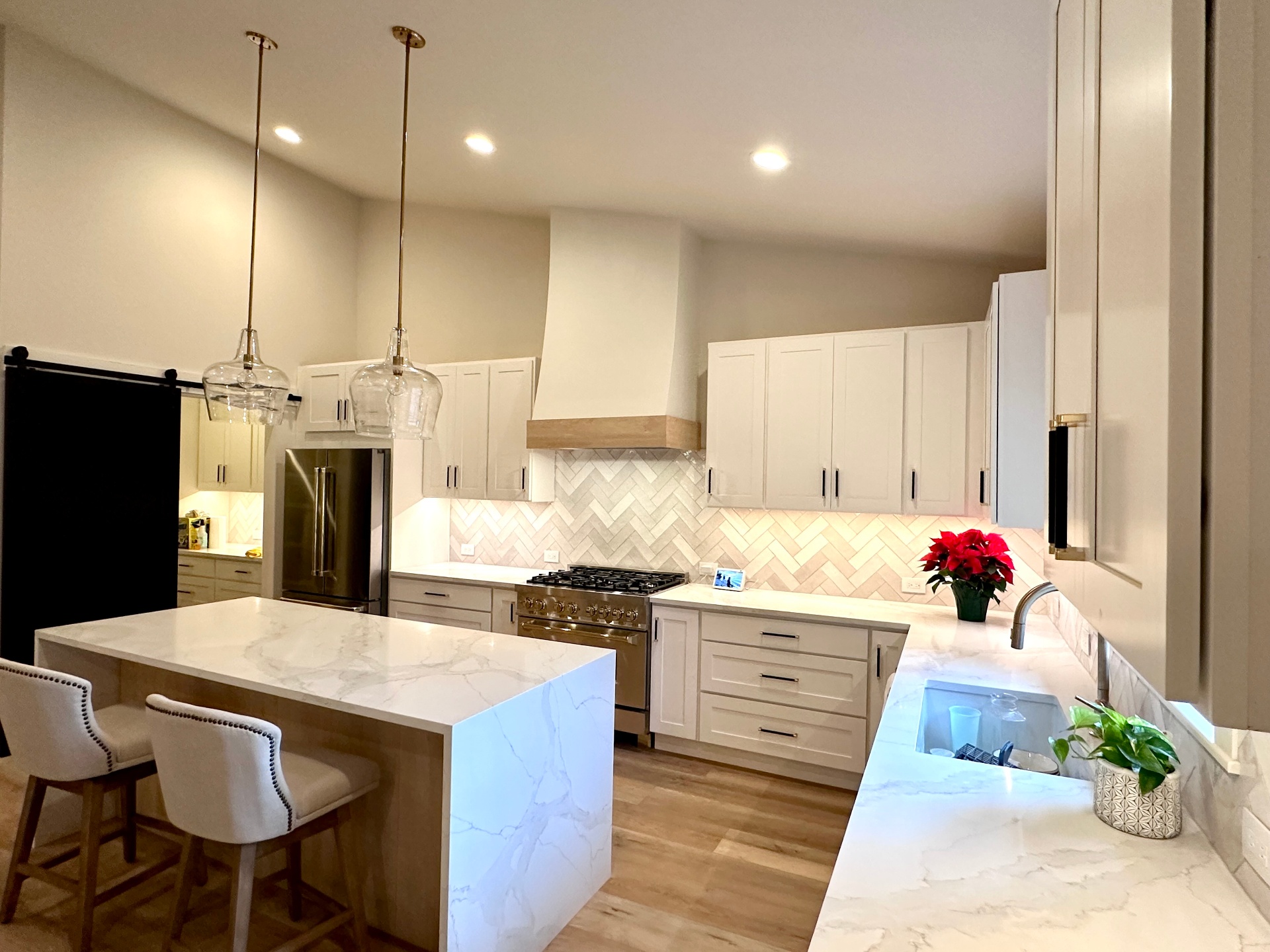 Modern white kitchen with waterfall island, pendant lights and herringbone tile
