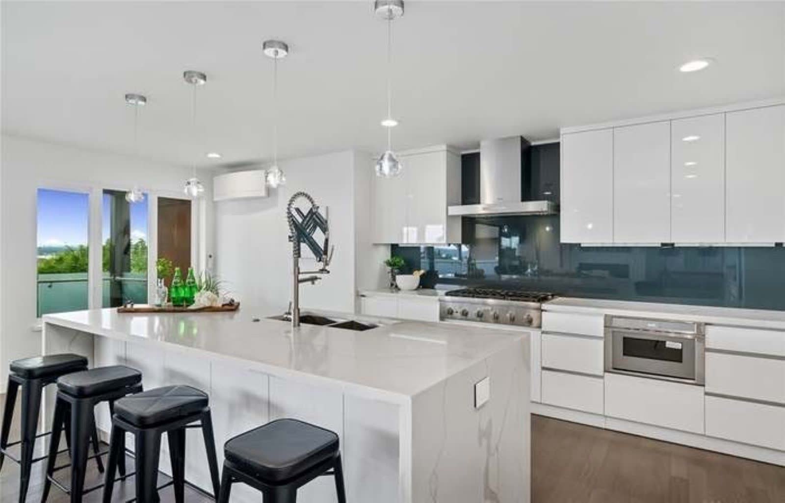 Contemporary white kitchen with long island, dark glass backsplash and sleek cabinetry