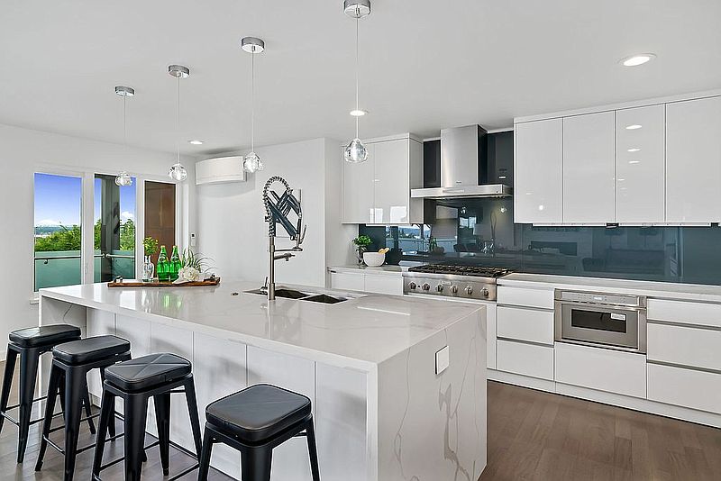 Modern white kitchen island with waterfall quartz counter and black bar stools