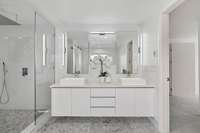White floating vanity with double vessel sinks, backlit mirrors and marble wall
