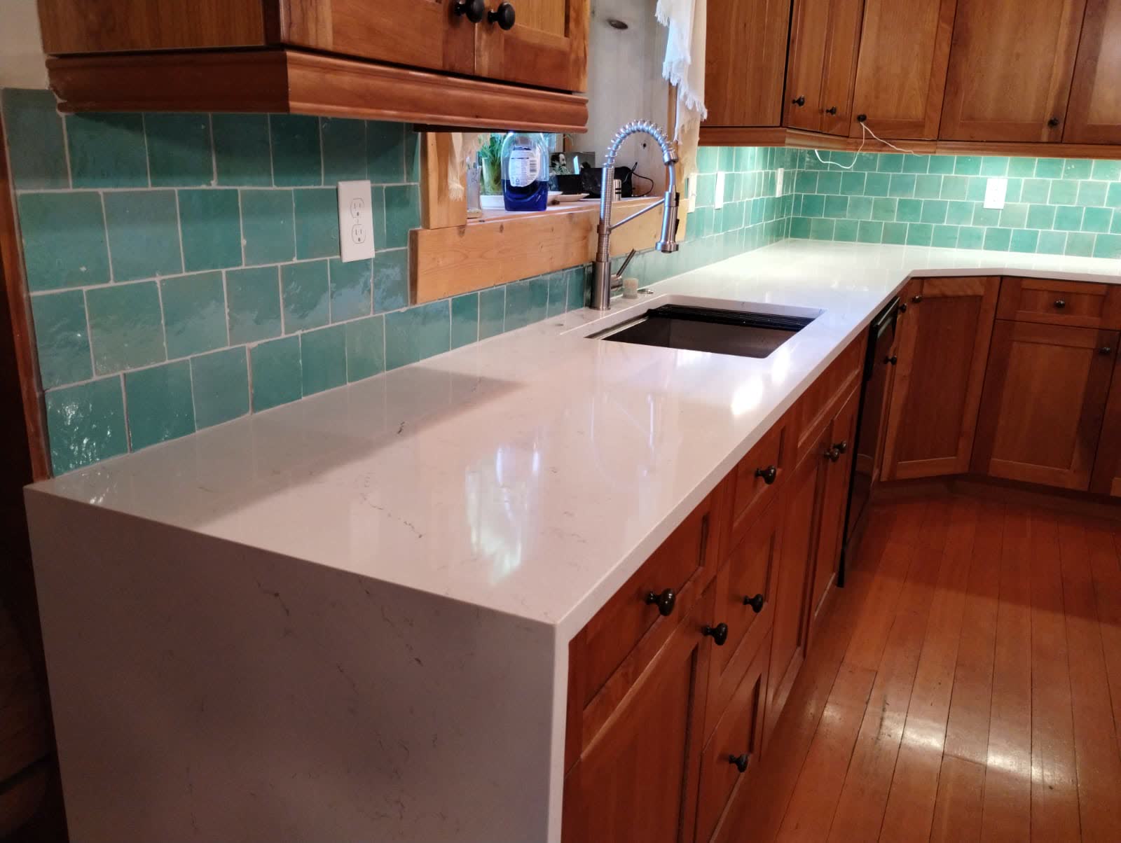 White quartz countertop with green subway tile backsplash and wood cabinets