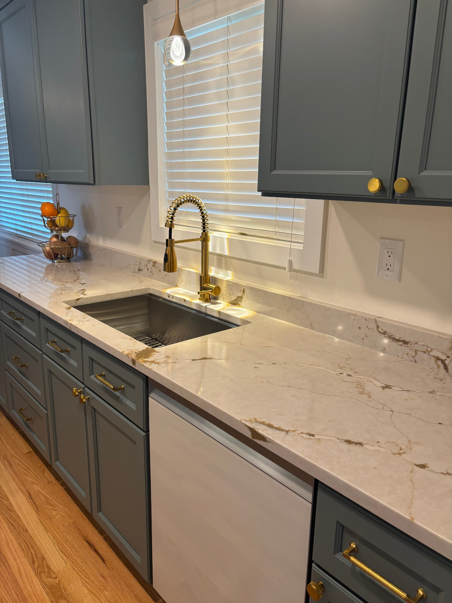 Close-up of gold-veined quartz counter with stainless sink and coiled brass faucet