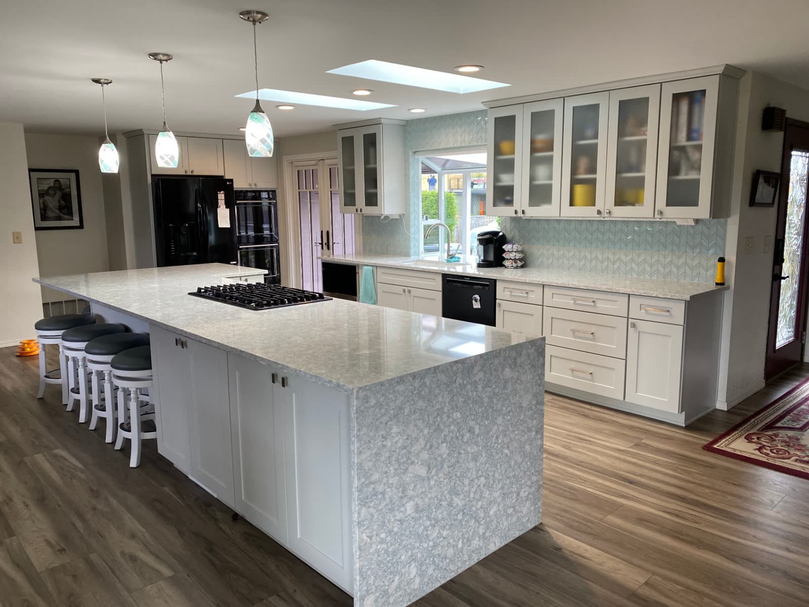 Expansive white shaker kitchen with oversized quartz waterfall island and chevron glass backsplash