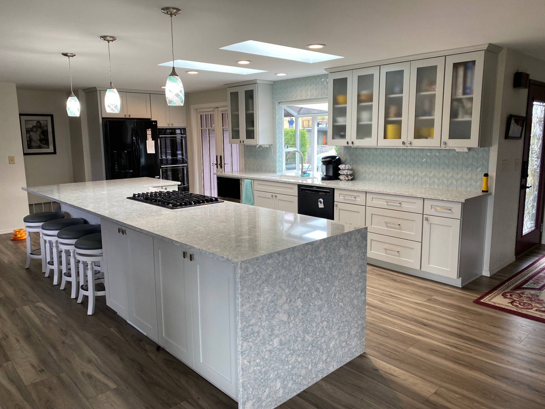 Expansive white shaker kitchen with oversized quartz waterfall island and chevron glass backsplash