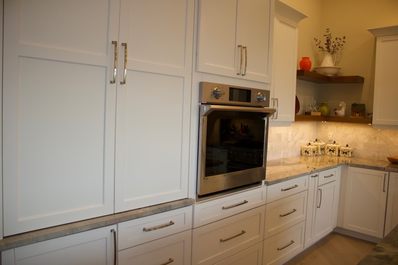 Floor-to-ceiling white shaker cabinetry with built-in wall oven and marble backsplash