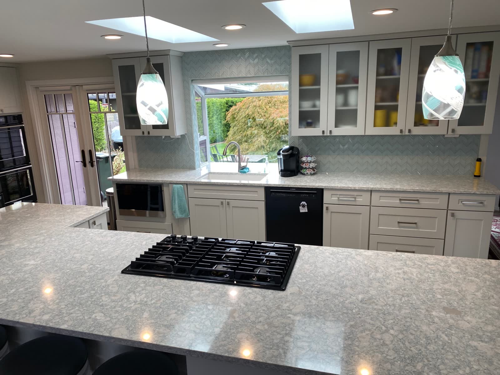 White shaker kitchen with skylights, chevron backsplash and quartz counters