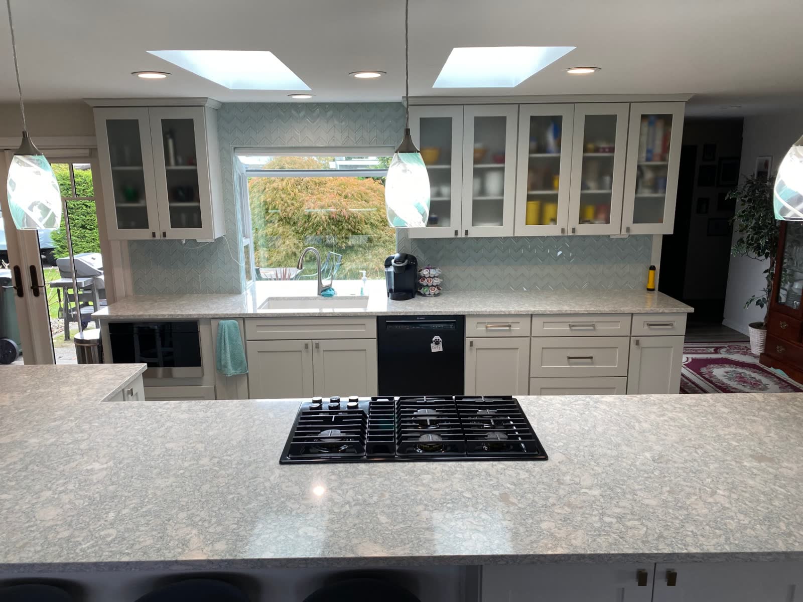 Bright white kitchen with dual skylights, glass-front cabinets and chevron backsplash