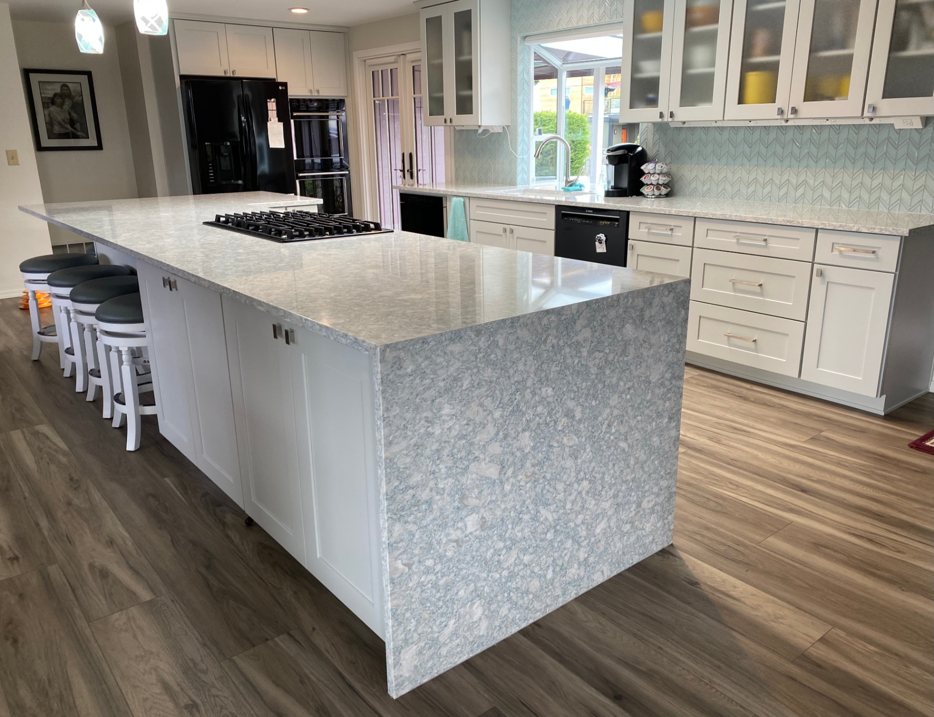Two-tier quartz island with waterfall edge, gas cooktop and rich wood flooring