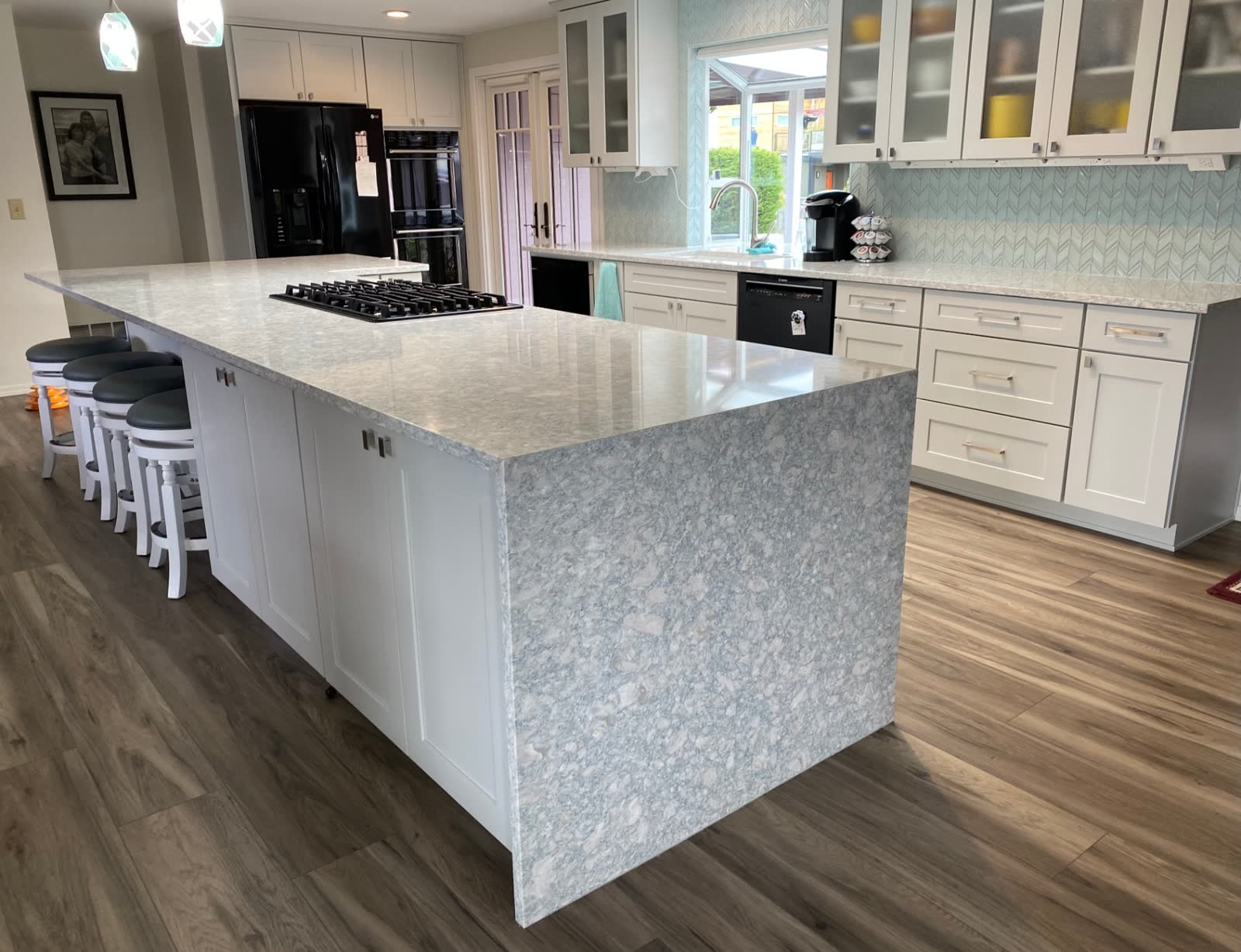 Two-tier quartz island with waterfall edge, gas cooktop and rich wood flooring