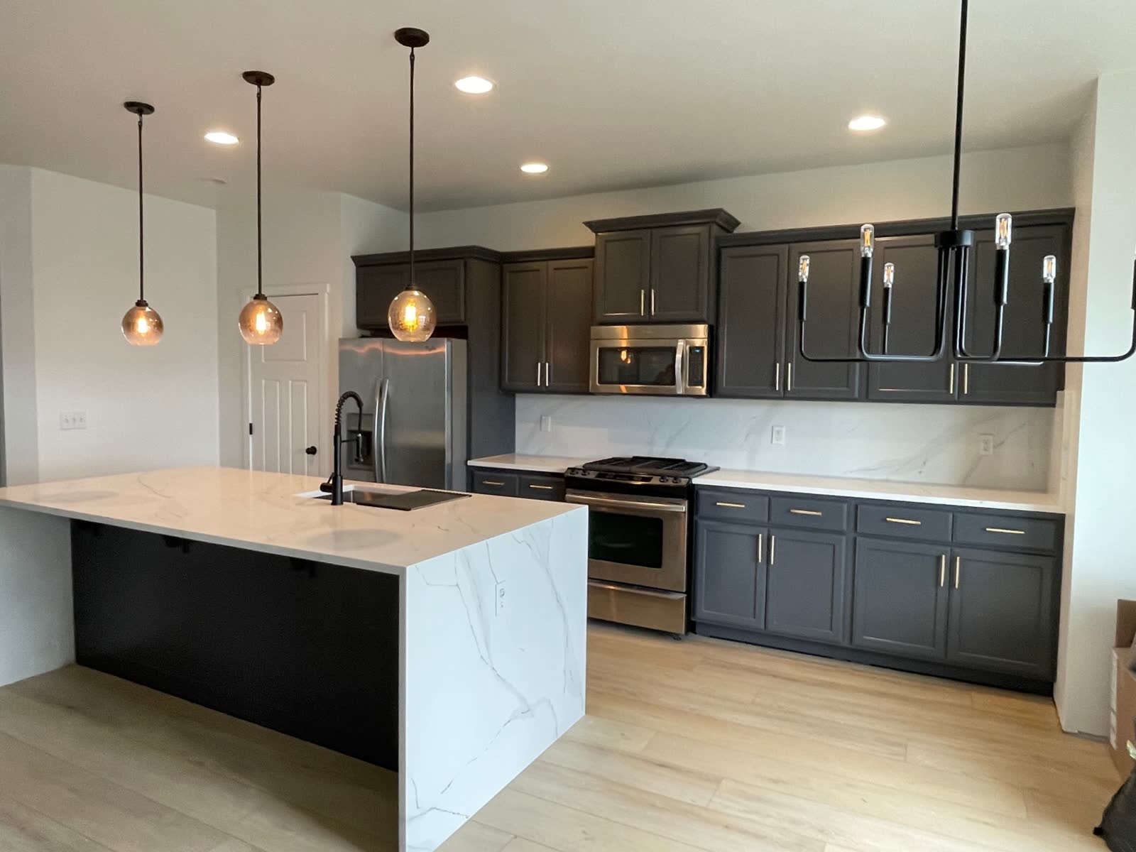 Modern kitchen with dark cabinets, calacatta waterfall island and bronze pendant lights