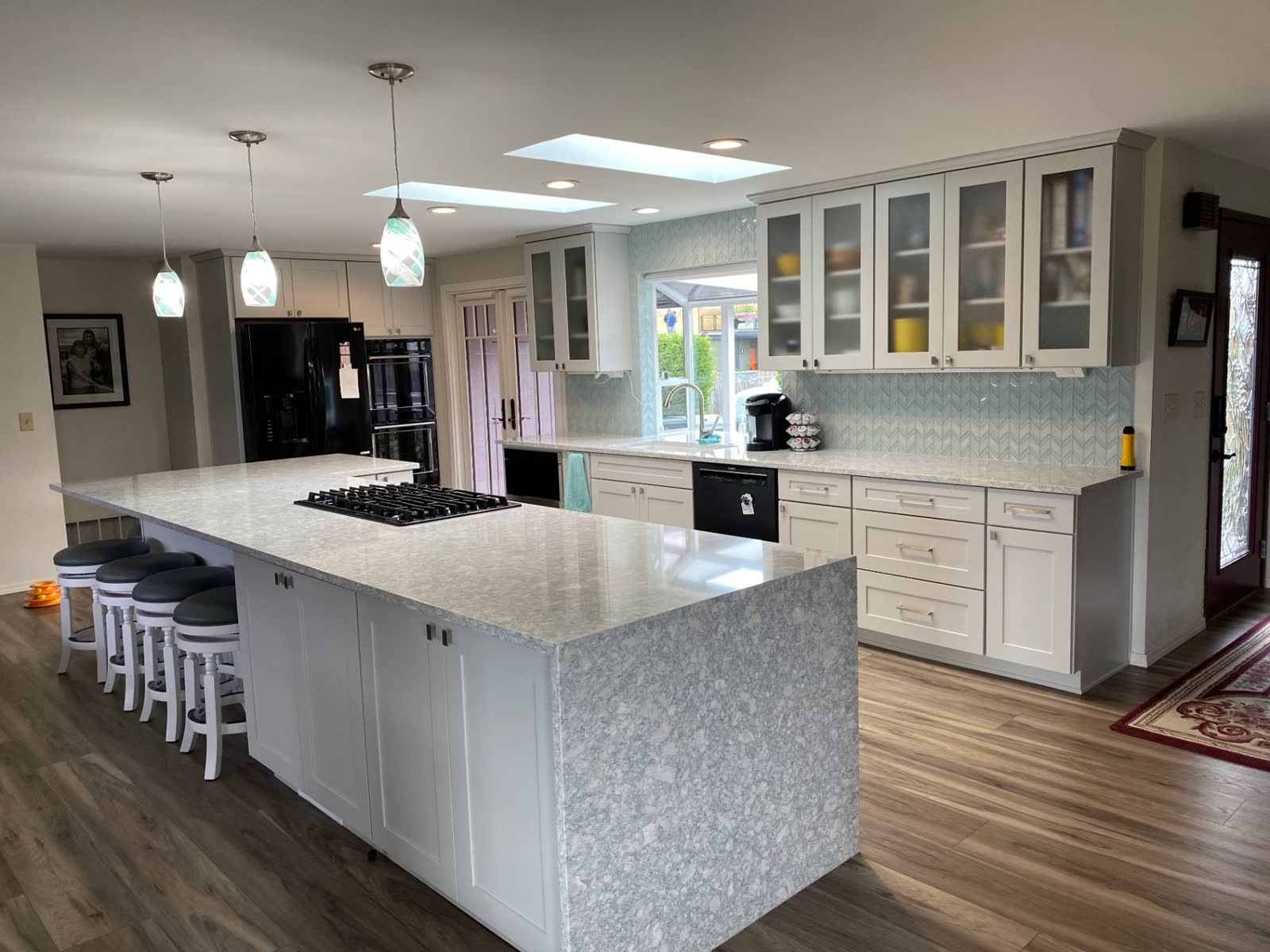 Spacious white kitchen with skylights, chevron mosaic backsplash and large quartz island