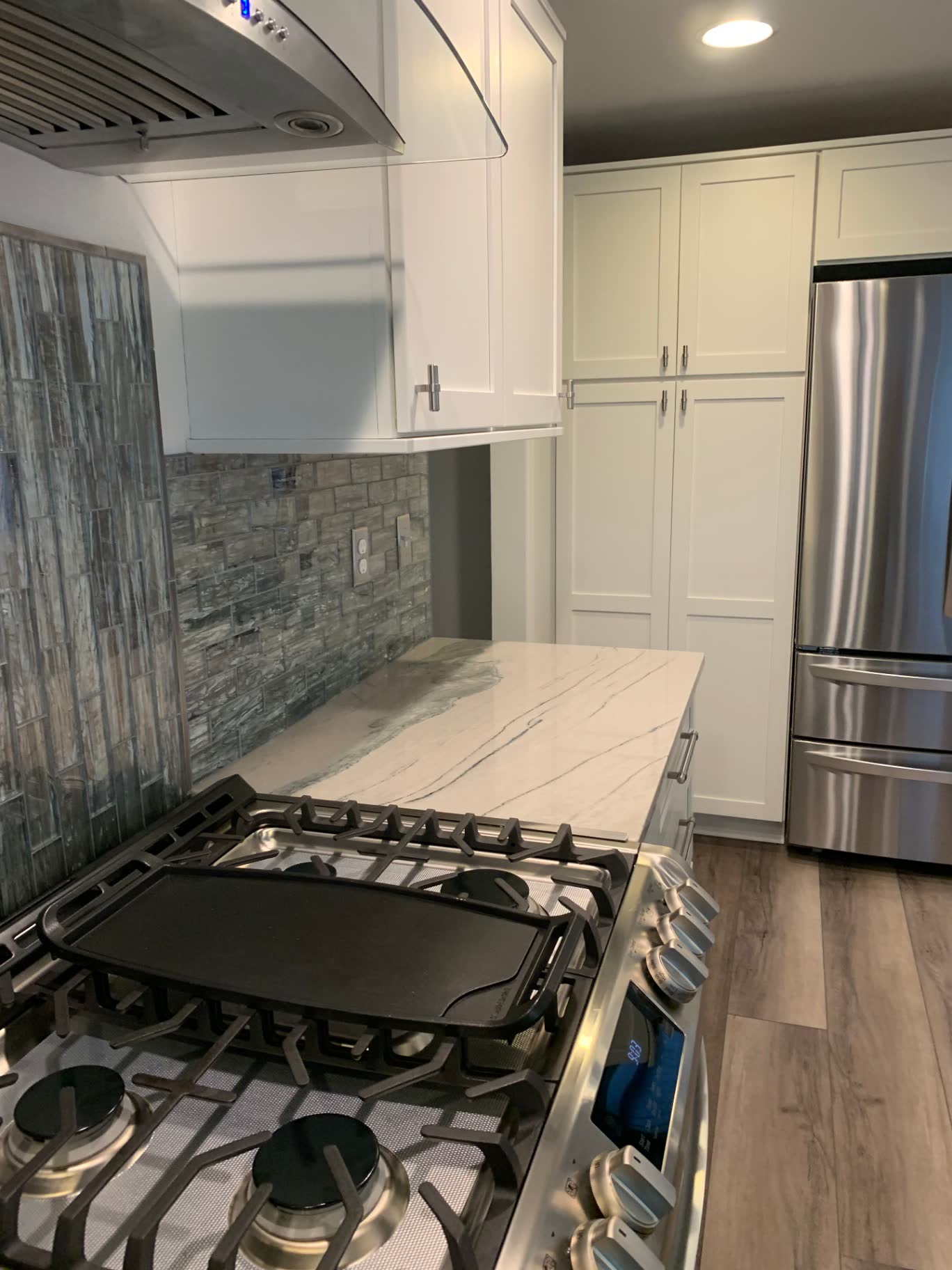 White shaker kitchen with quartzite counters and iridescent glass tile backsplash