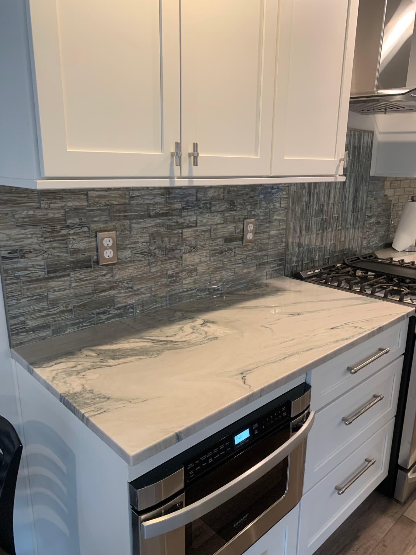 Quartzite countertop with dark glass mosaic backsplash and stainless microwave drawer