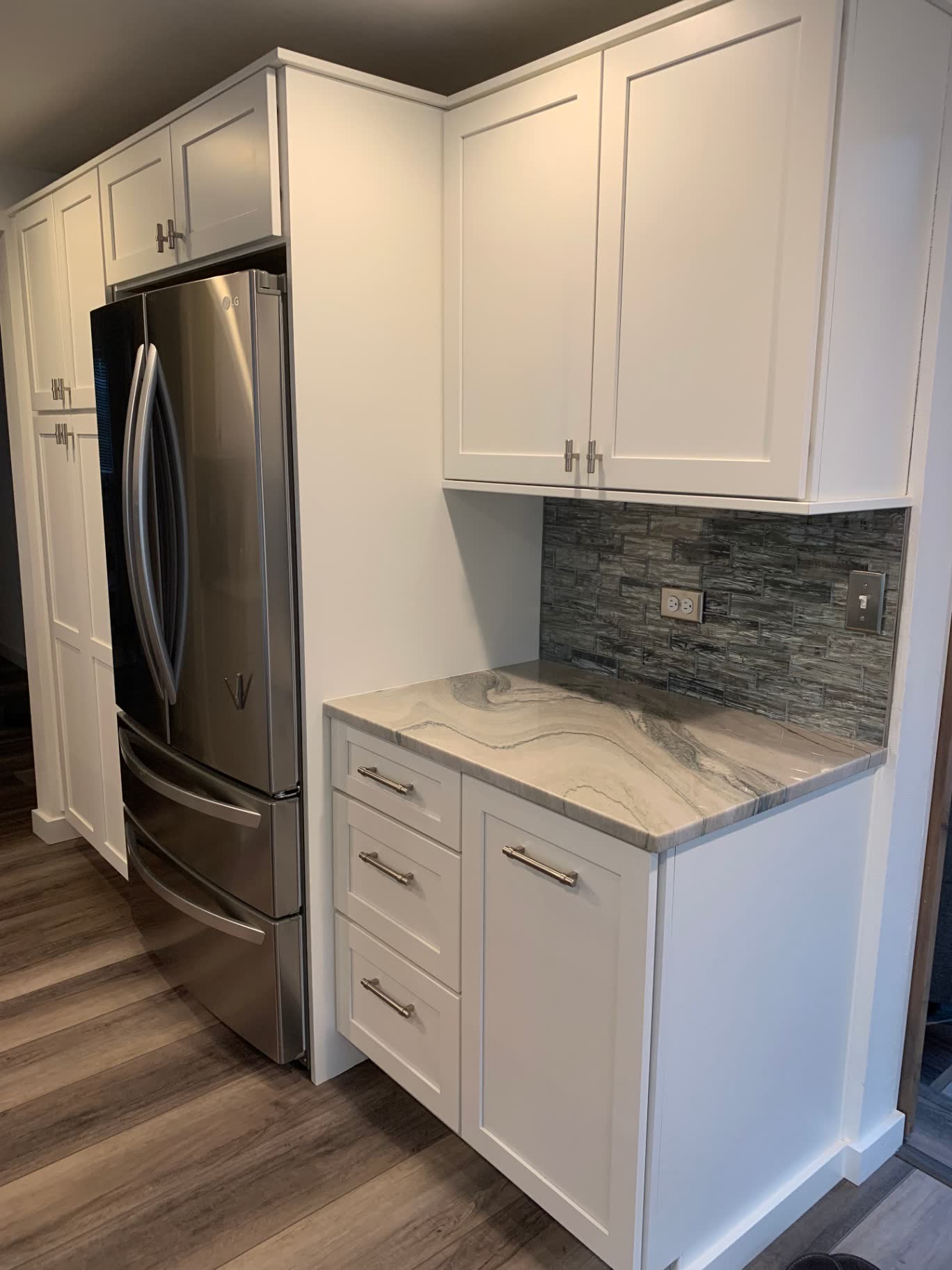White shaker cabinets flanking a stainless refrigerator with quartzite counter