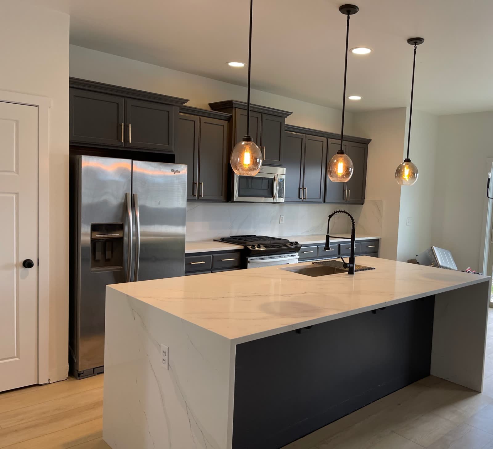 Contemporary kitchen with dark cabinets, marble backsplash and waterfall island