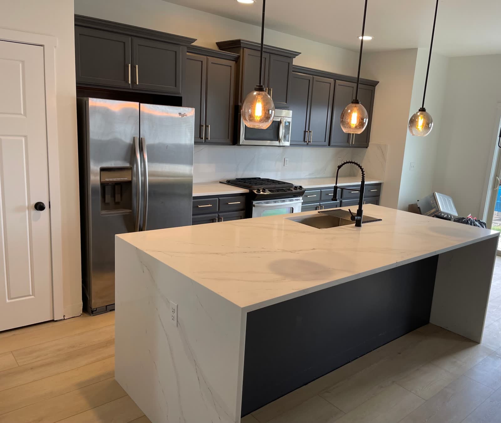 Dark cabinet kitchen with white marble backsplash and calacatta waterfall island