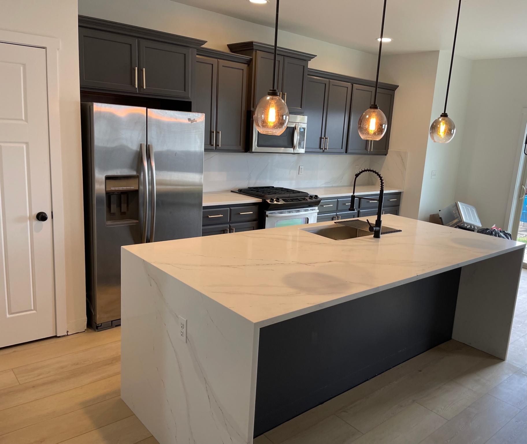 Dark cabinet kitchen with white marble backsplash and calacatta waterfall island