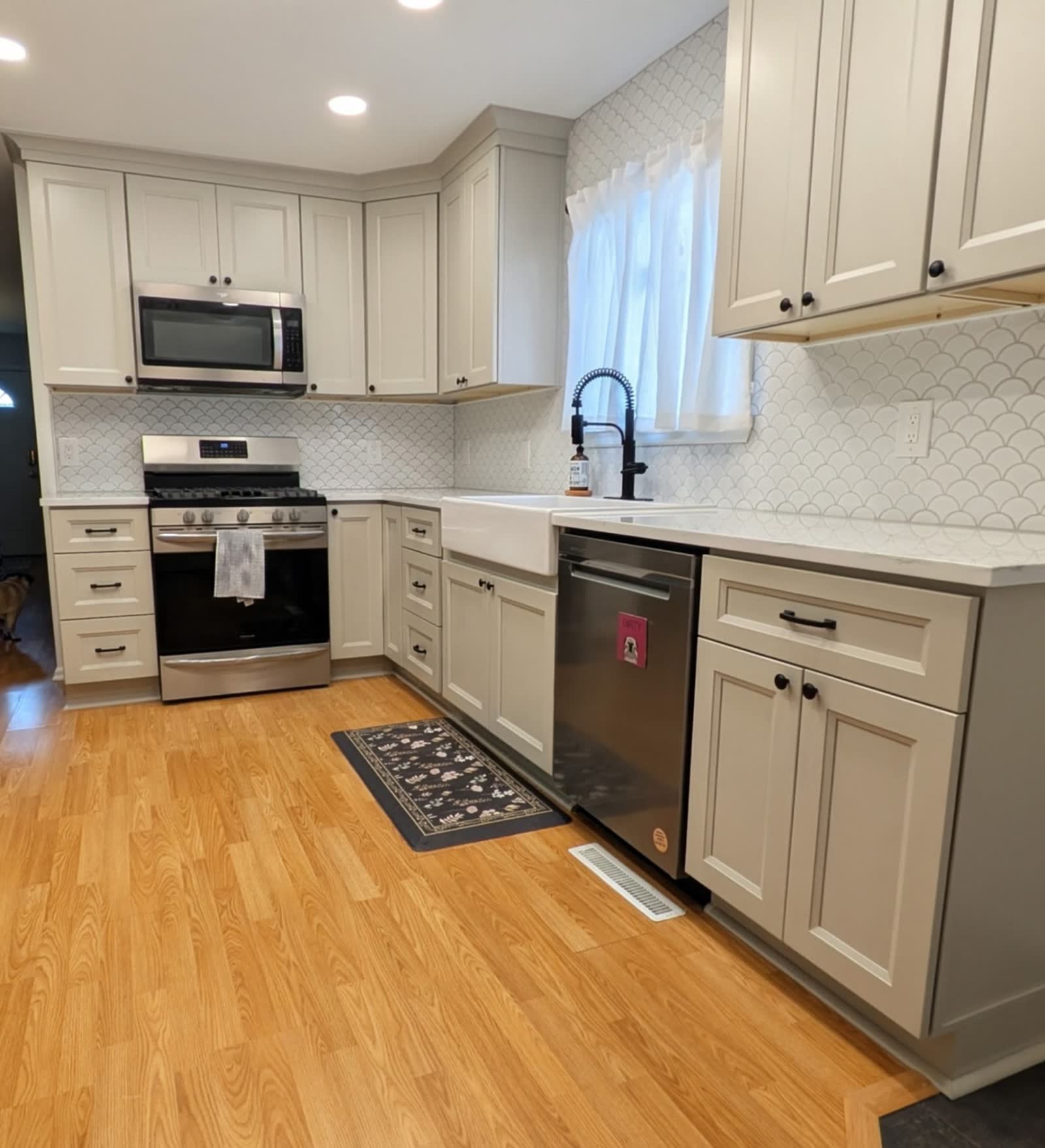 Greige shaker kitchen with fish-scale tile backsplash and farmhouse sink.