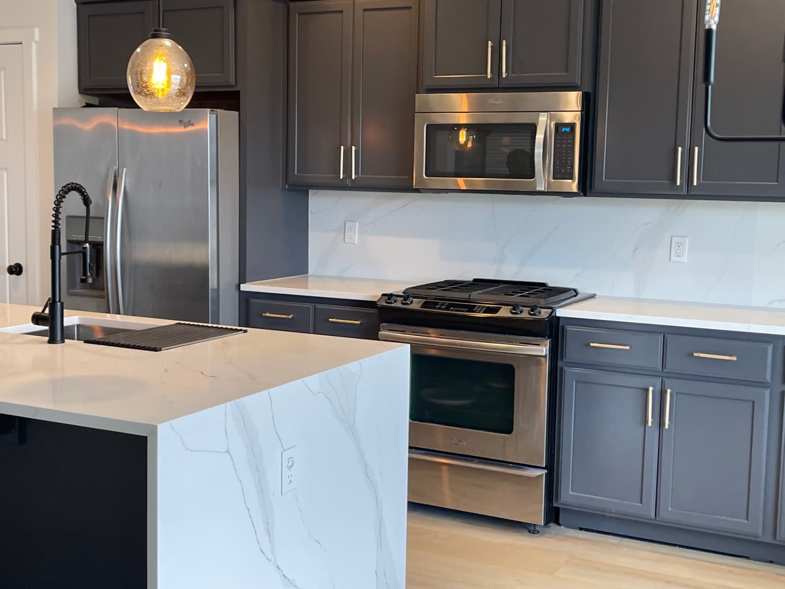 Dark cabinets with marble backsplash, stainless appliances and quartz waterfall island