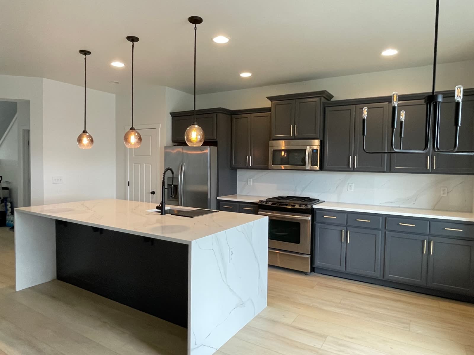 Open-concept kitchen with dark cabinets, calacatta waterfall island and bronze pendant lights