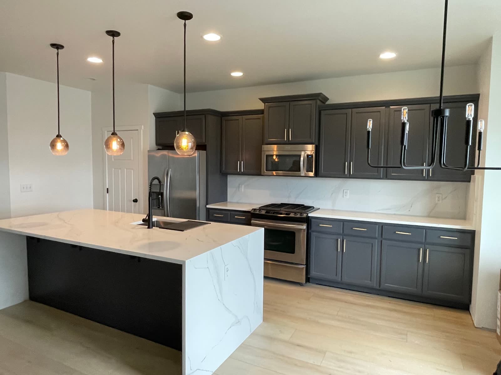 Dark shaker kitchen with quartz waterfall island and linear chandelier over island