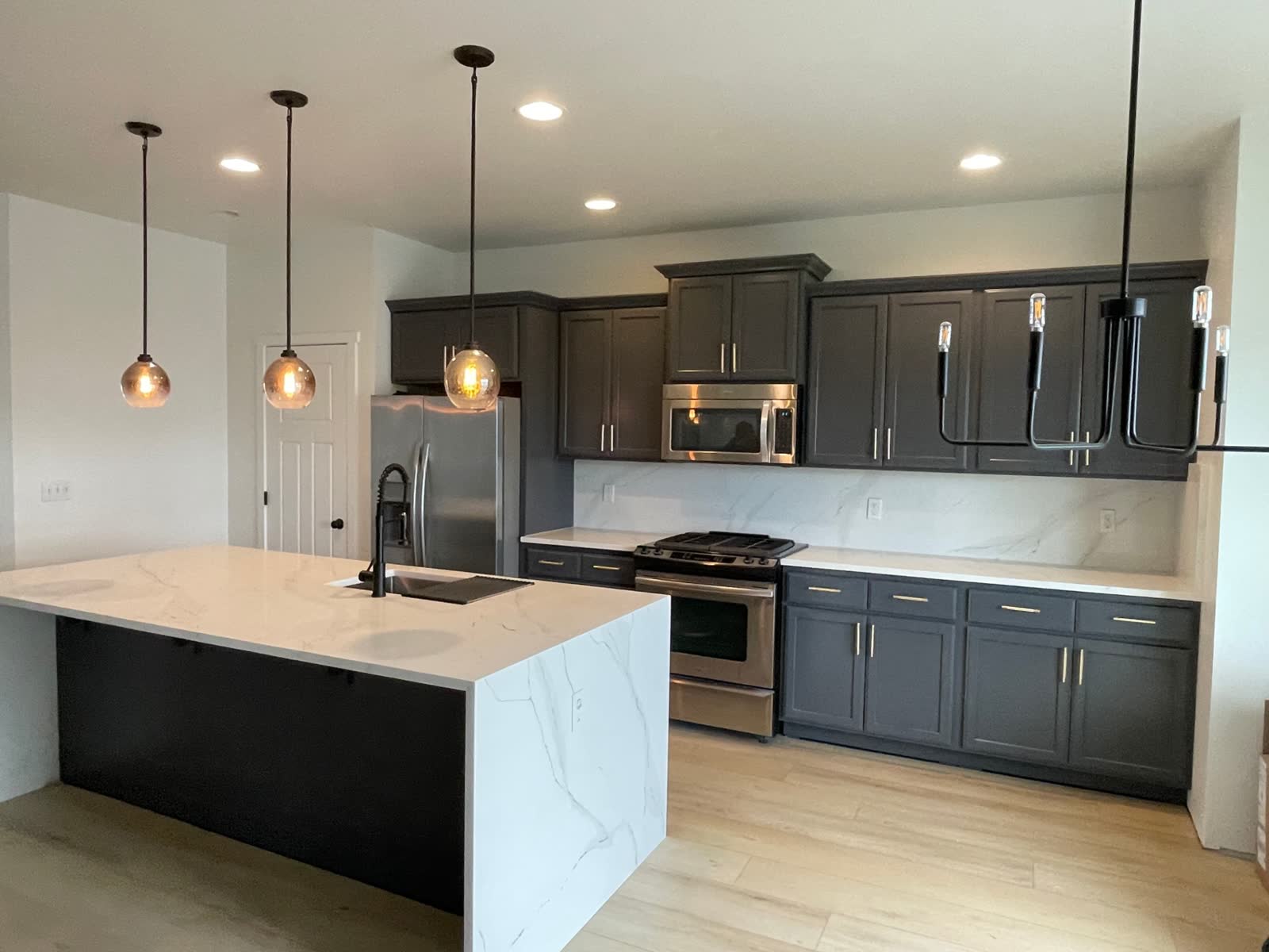 Contemporary dark cabinet kitchen with marble backsplash and waterfall island