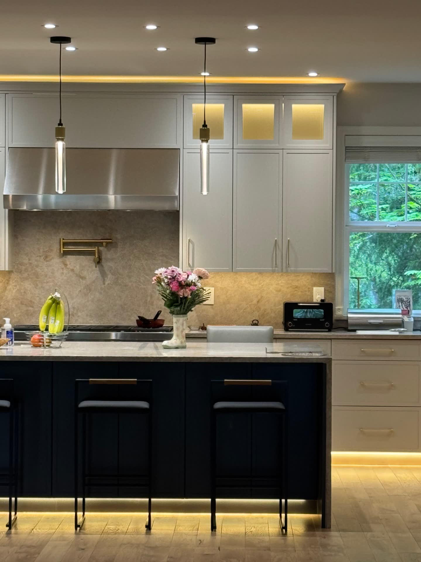 Sophisticated kitchen with light cabinets, brass pot filler and navy island with LED accent lighting
