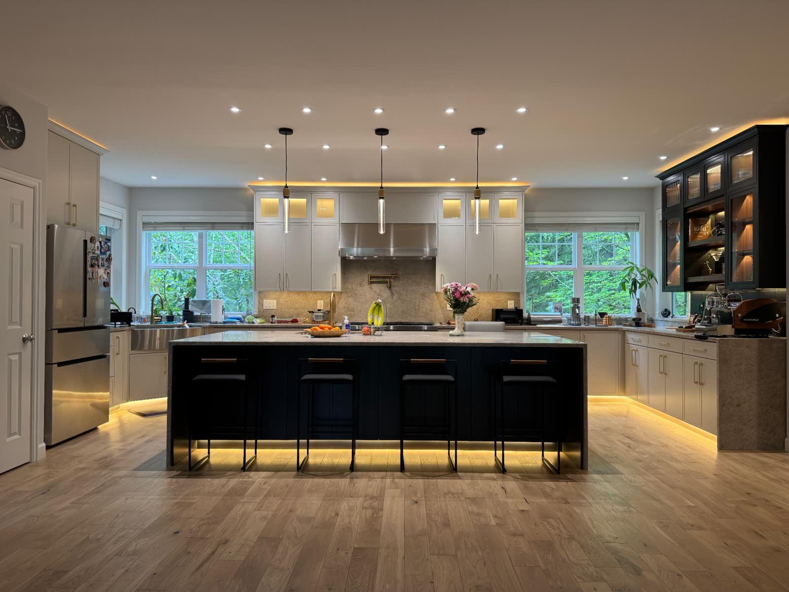 Expansive kitchen with navy island, stainless hood and glass-front upper cabinets with LED cove lighting
