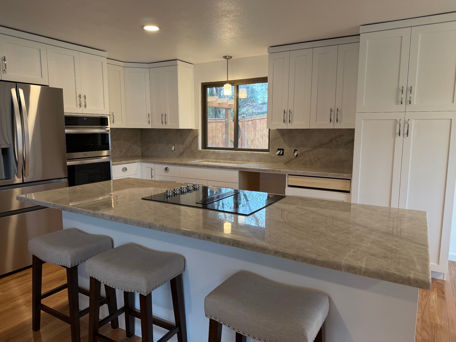 Bright white kitchen with quartzite waterfall peninsula, cooktop and upholstered stools