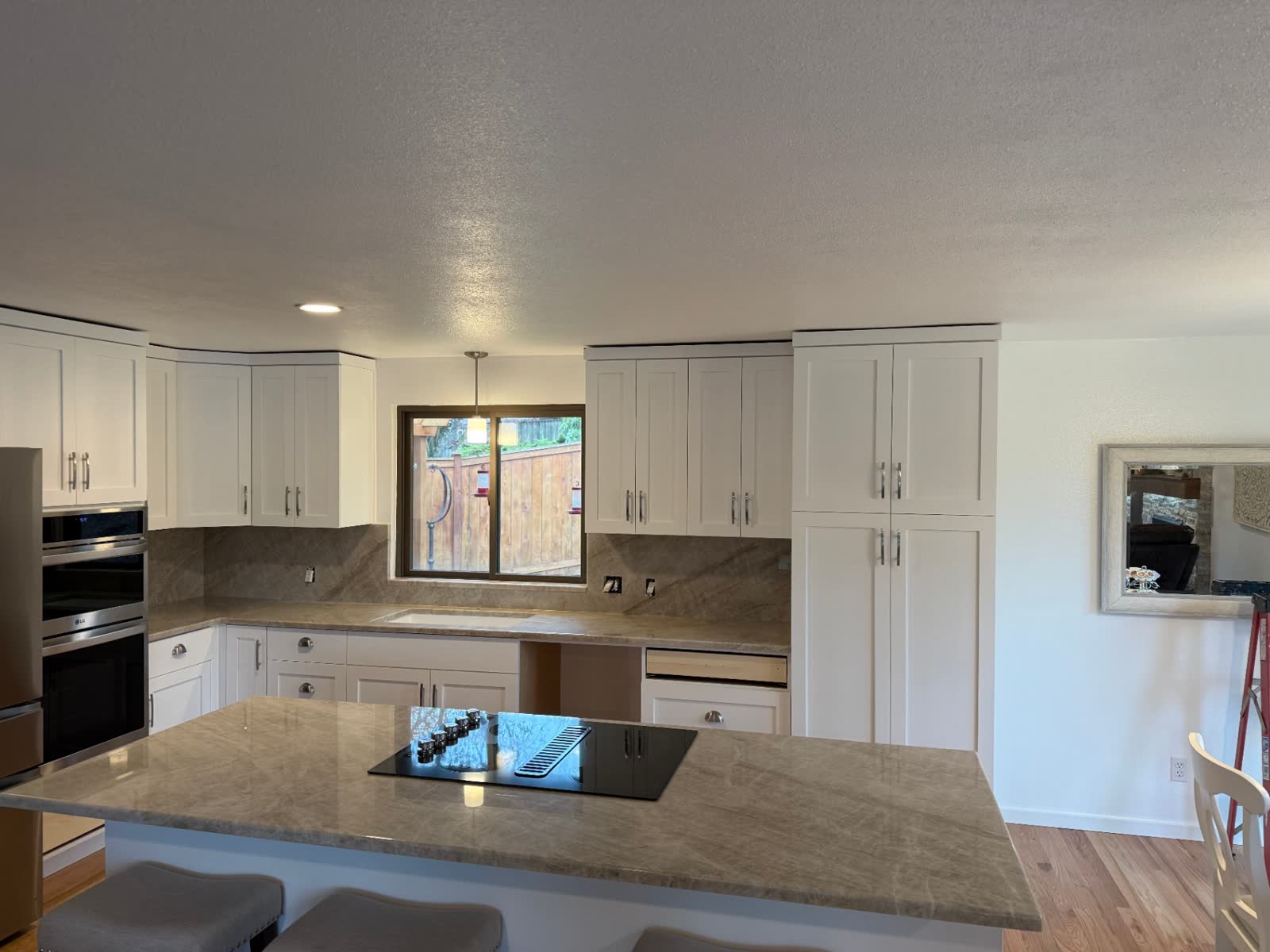 White shaker kitchen with quartzite backsplash and peninsula overlooking backyard