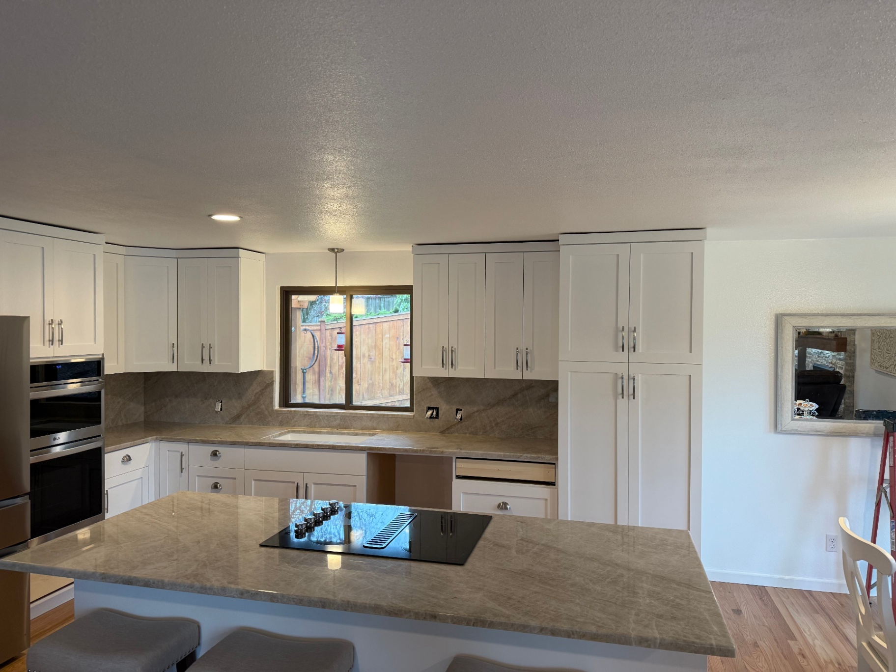 White shaker kitchen with quartzite backsplash and peninsula overlooking backyard