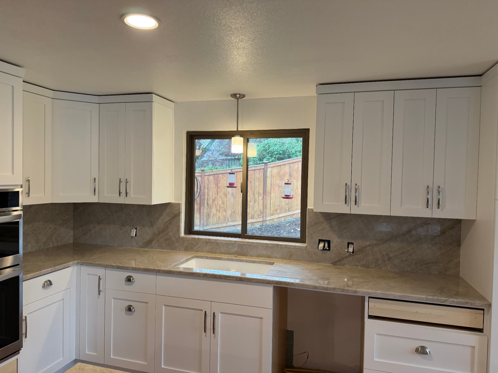 White shaker kitchen with quartzite backsplash and stainless double oven
