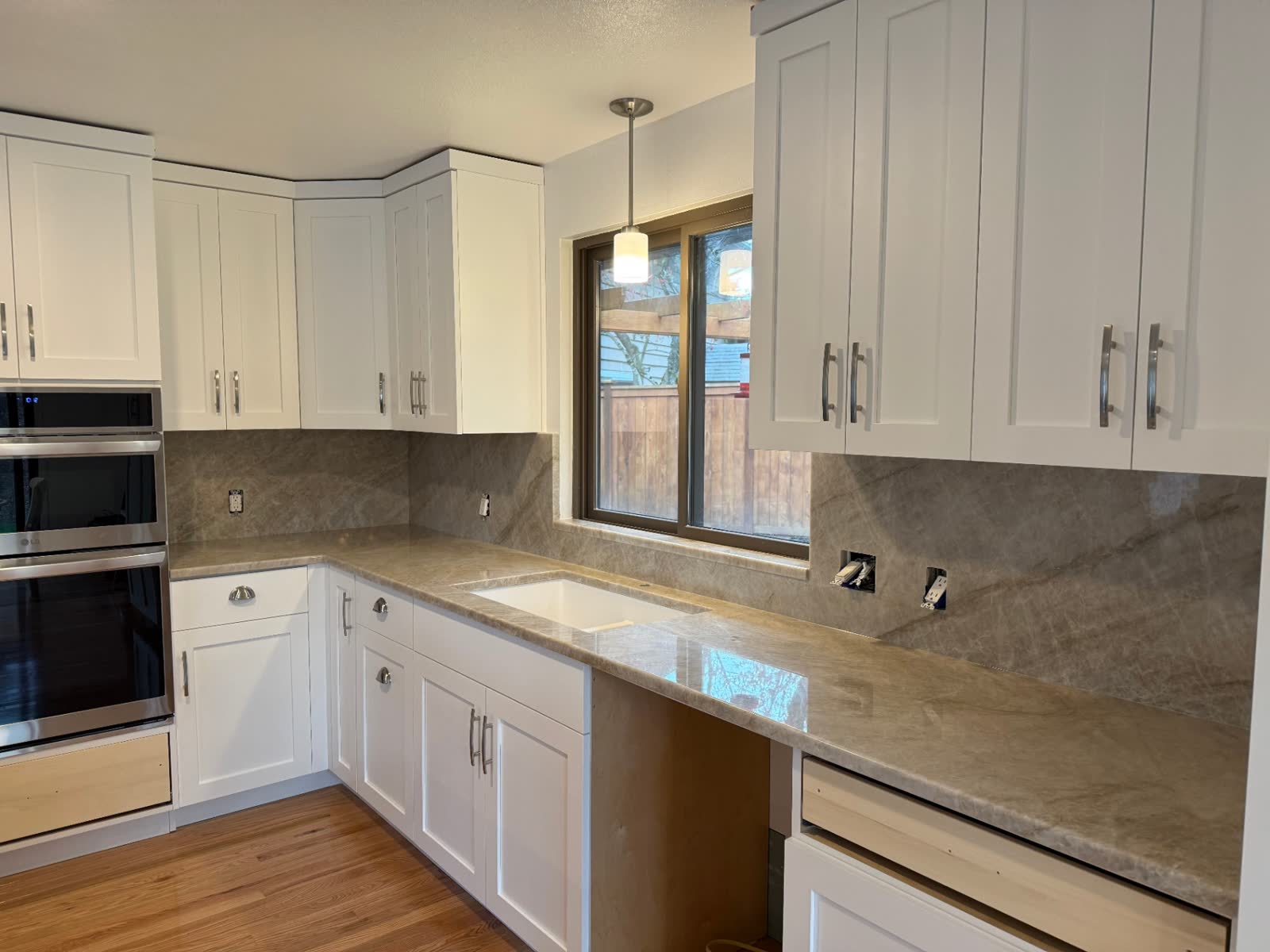 L-shaped white kitchen with taj mahal quartzite counters and farmhouse sink