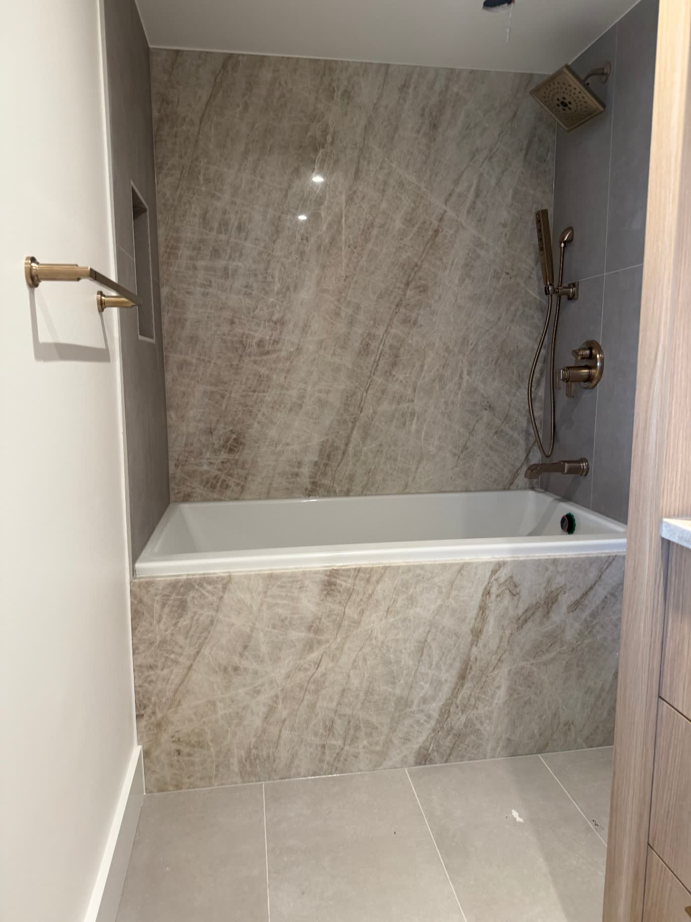 Guest bath with quartzite tub surround, tile floor and brushed bronze fixtures.