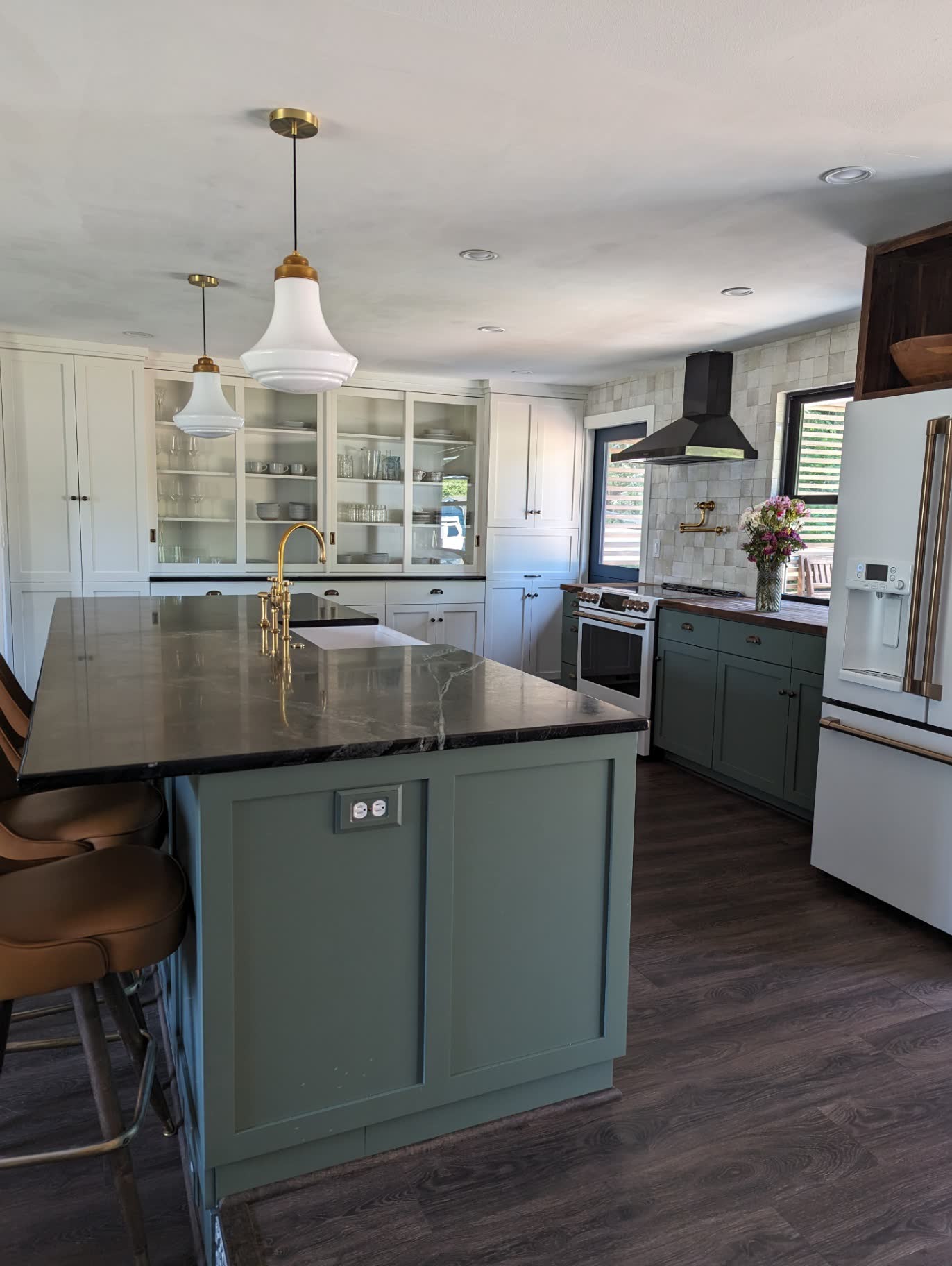 Sage green island kitchen with soapstone counters, glass cabinets and brass fixtures