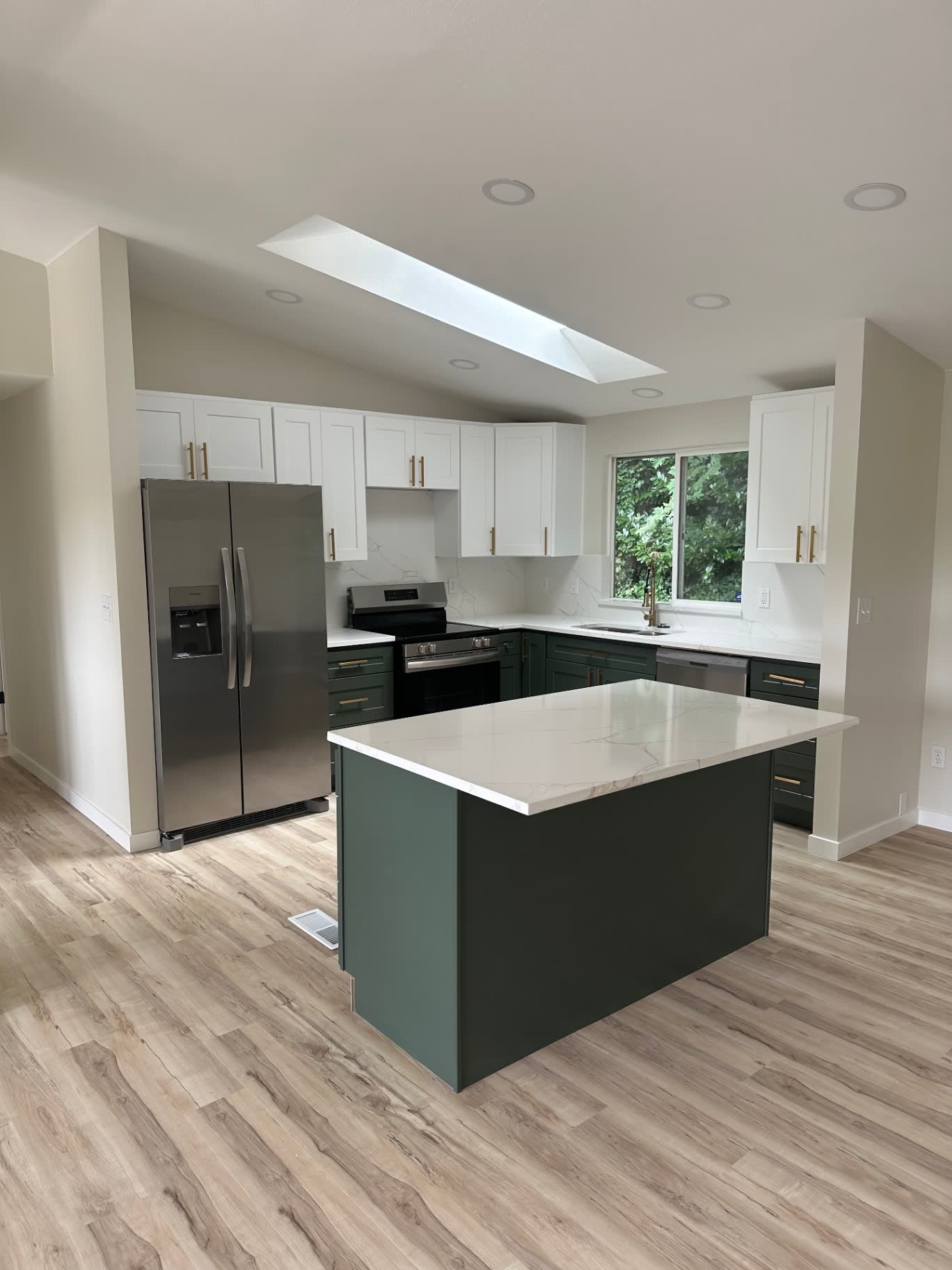 Two-tone kitchen with dark green base cabinets, white uppers and skylight