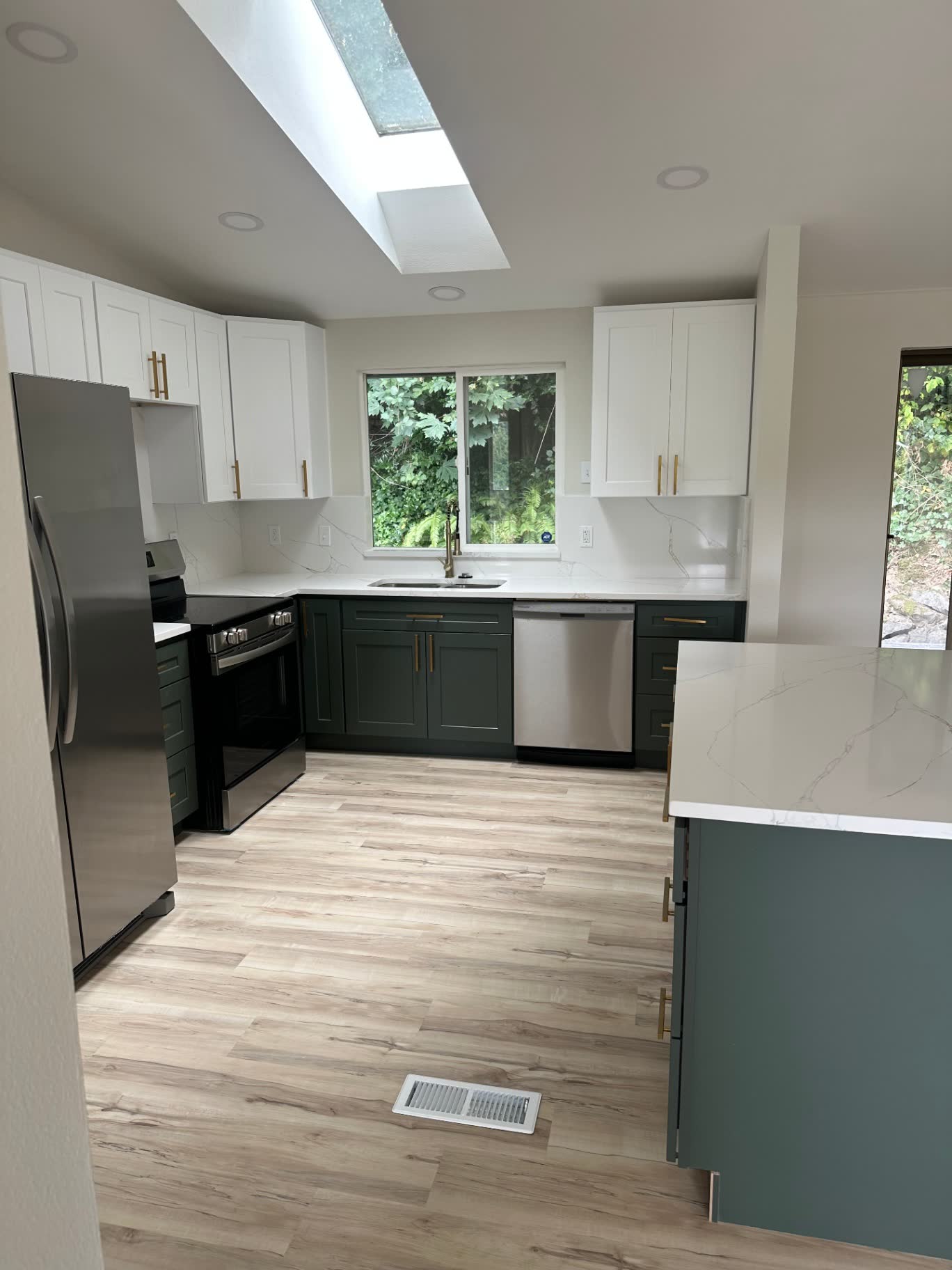 Contemporary kitchen with dark green cabinets, quartz waterfall island and vaulted skylight