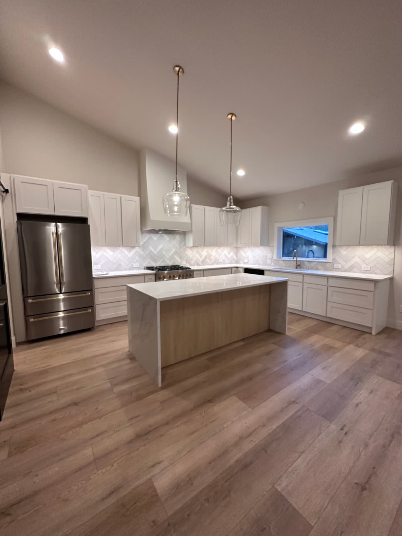 Vaulted white kitchen with herringbone marble backsplash.