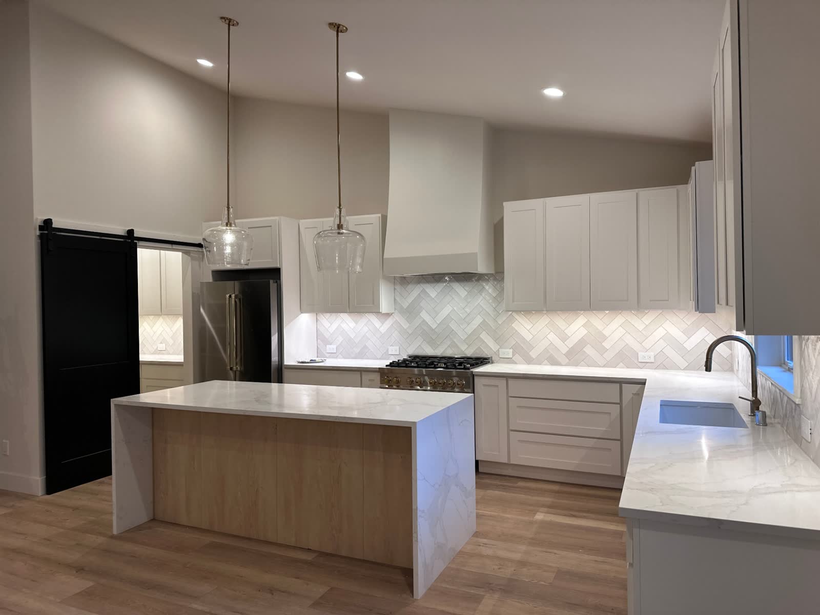 Bright white kitchen with plaster hood, black barn door and marble waterfall island