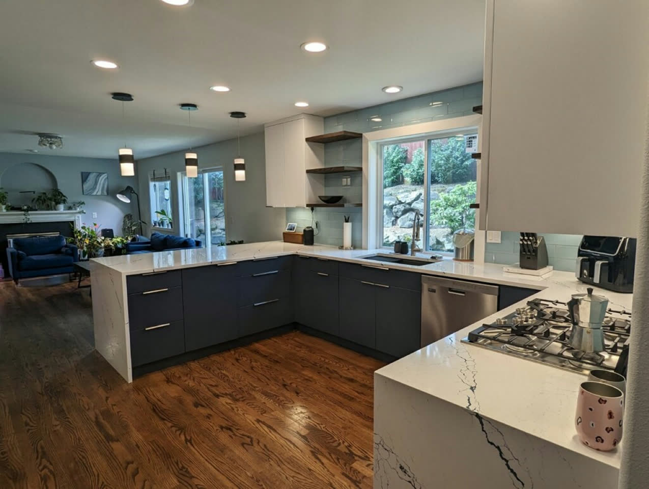 Modern open kitchen with navy cabinets, calacatta quartz waterfall peninsula and floating shelves