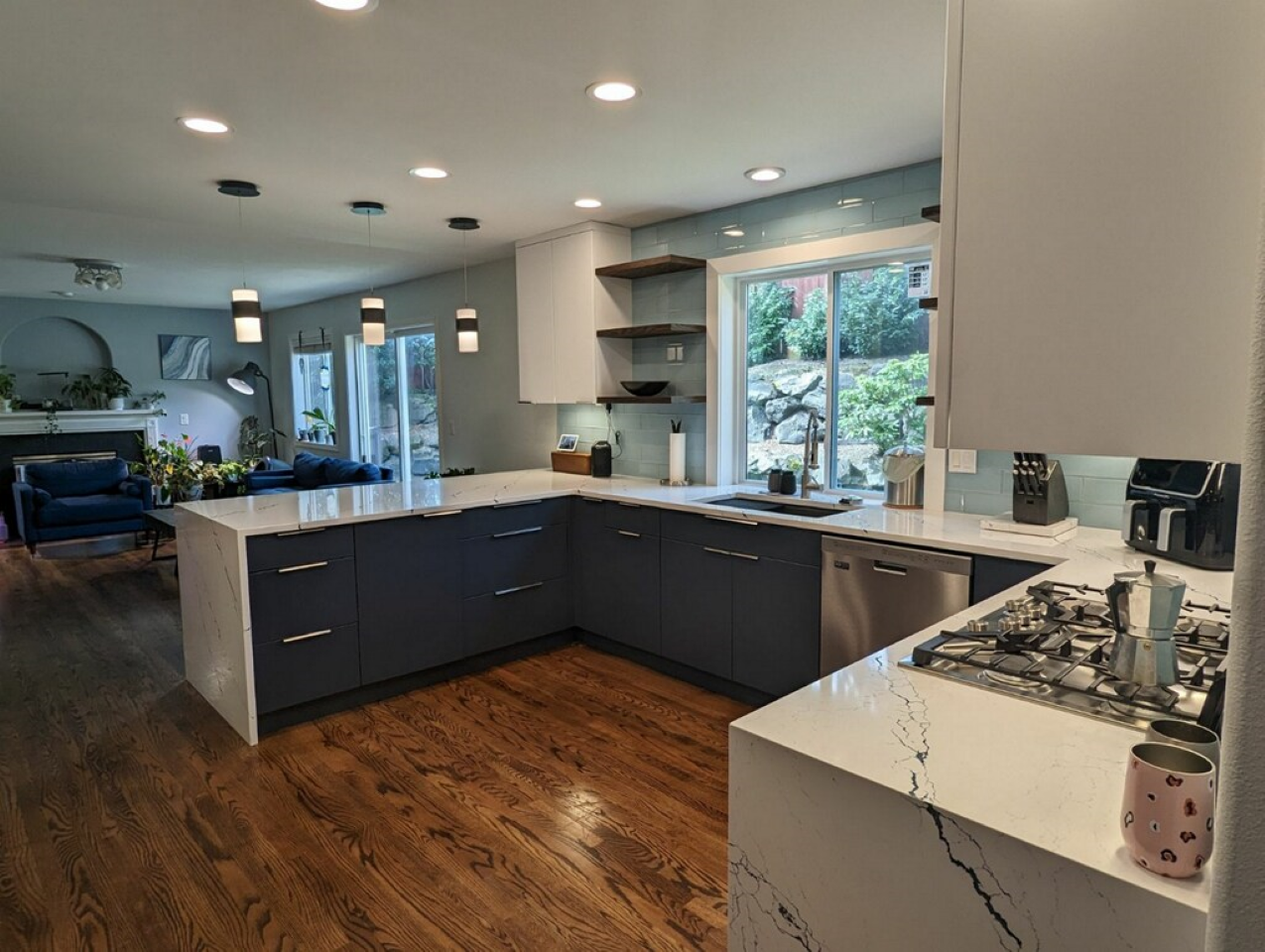 Modern open kitchen with navy cabinets, calacatta quartz waterfall peninsula and floating shelves