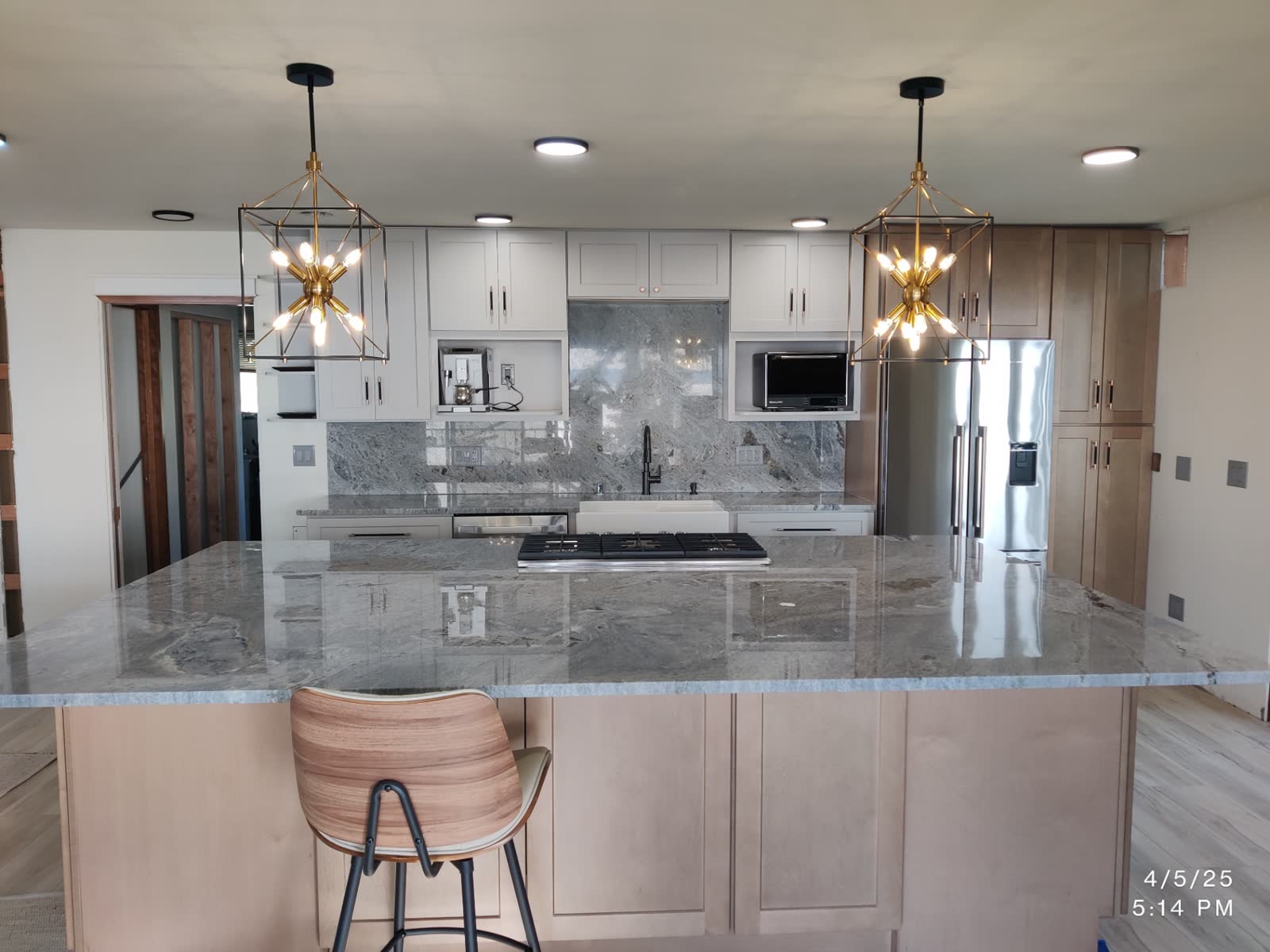 Two-tone kitchen with maple island, geometric brass pendants and dramatic granite backsplash