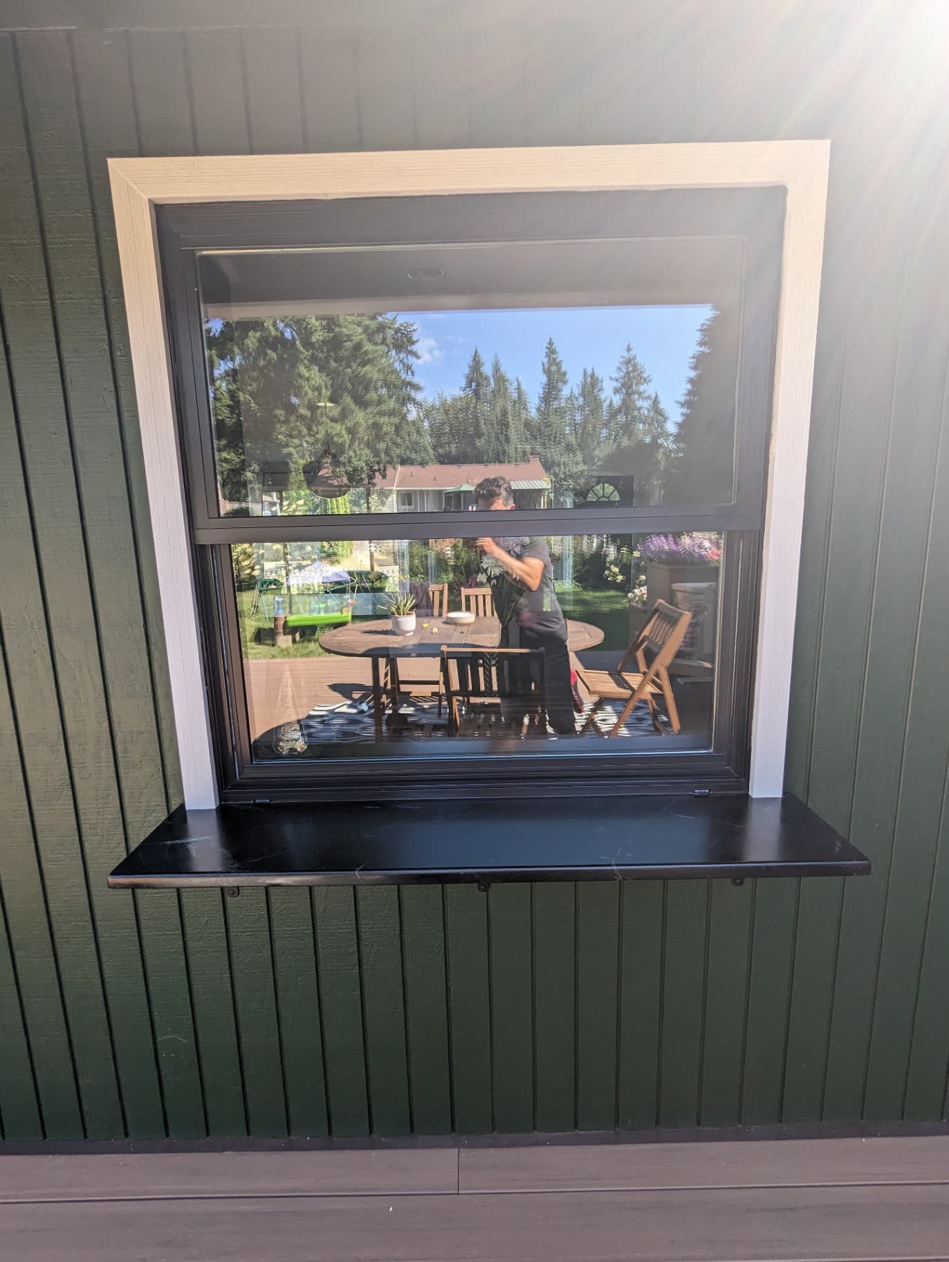 Dark green board-and-batten exterior with black-framed picture window and soapstone sill